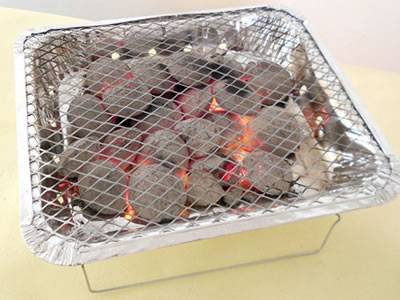 A disposable barbecue grill on cooker and several charcoals in the cooker.