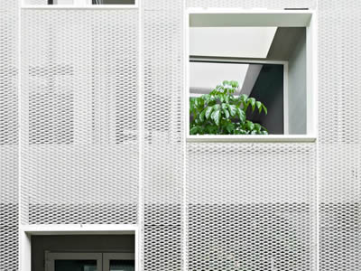 Expanded metal facade with two square window, there was a person lean on a window, the other one shows some green leaves.
