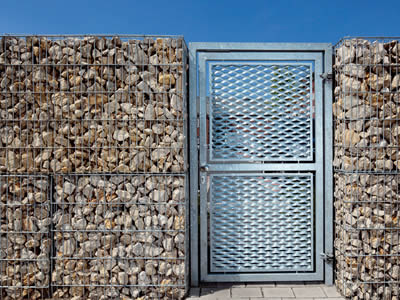 Puerta metálica expandida utilizada en la casa, y vallas de gaion junto a la puerta metálica expandida.