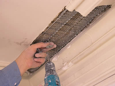一隻手試圖使用工具將螺釘安裝在膨脹的石膏網中。